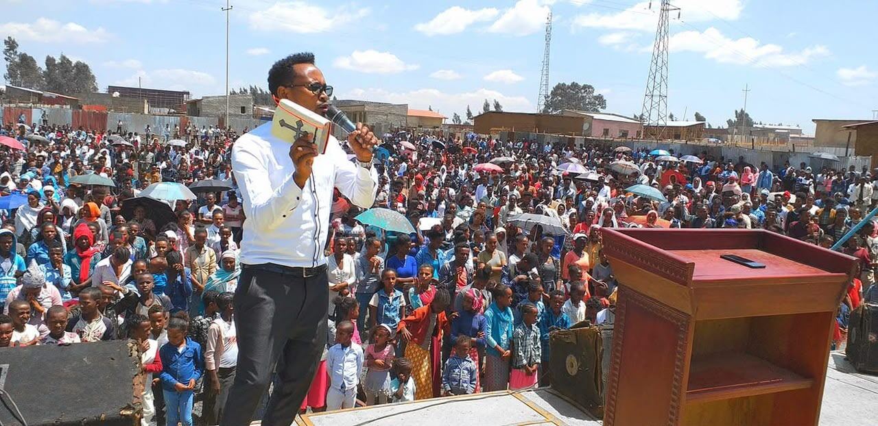 Evangelist preaching with a Bible in hand before a wide crowd